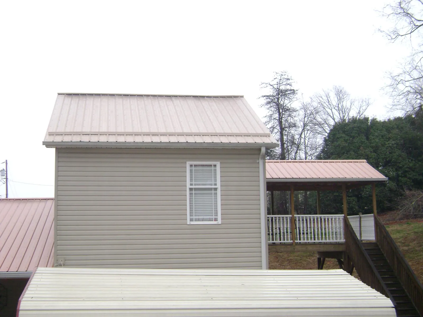 Tan metal roofs on a two story addition and attached porch, from a Roof Replacement job in Clayton